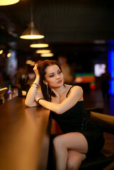 Beautiful brunette woman in evening dress posing near bar alone