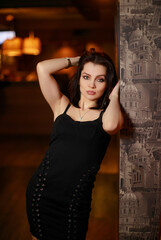 Fototapeta premium Gorgeous beauty young brunette woman in black dress posing at the bar
