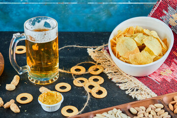 Assorted snacks, chips and a glass of beer on dark table