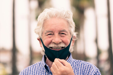 Coronavirus. White-haired senior man takes off the protective face mask to smile at camera.