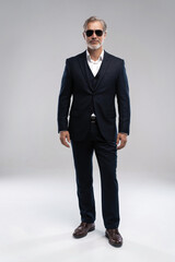 Full length shot of a respectable mature man in a suit and sunglasses on a gray background....