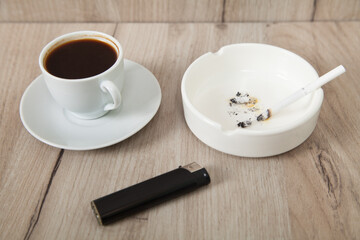 Ashtray, lighter, cigarette and coffee on a wooden background.