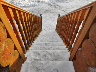Snow-covered wooden stairs with carved handrails descend
