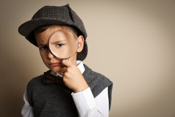 Little boy with magnifying glass playing detective on beige background. Space for text