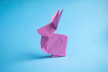 Step-by-step instructions for creating  origami bunny out of colored paper on  blue background, for  decorative Easter party decoration or for small Easter gifts.