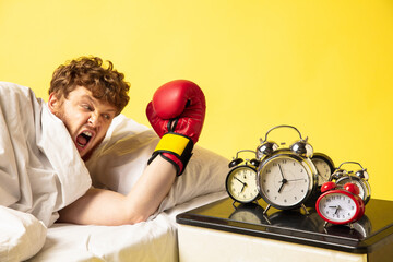 Punch. Man wakes up at his bed on yellow background and he's mad at clocks ringing, switches it off...