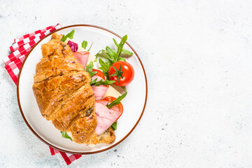 Croissant sandwich with ham, cheese and fresh salad in white plate. Top view with copy space on white stone table.