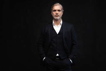 Handsome middle-aged man in suit posing against black background