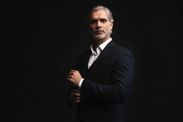 Handsome middle-aged man in suit posing against black background