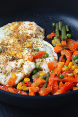 fried eggs and vegetables in a black frying pan, close-up, space for text