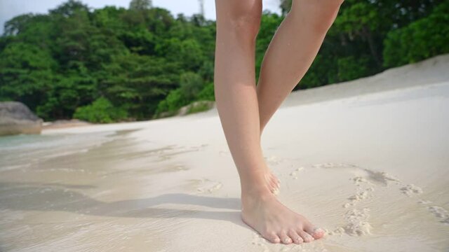 Young woman legs walking on white sand island beach with blue sea water, splashing ocean wave, hot and sunny weather, tropical summer vacation, Asia Pacific travel destination, front view low angle