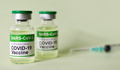 COVID-19 (SARS-CoV-2) coronavirus vaccine bottle with blurred syringe on green background banner. Focus on front bottle