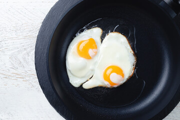 fried eggs in a black frying pan on a light wooden table, close-up, space for text
