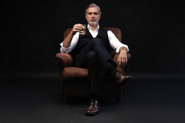Portrait of handsome elegant mature man with a glass whiskey in a dark room.