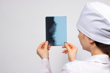 A doctor in white uniform examines an X-ray of a patient with a broken nose bone. Nose injury, crack or fracture - radiology and traumatology.