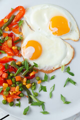 Fried eggs and vegetables in a white plate.