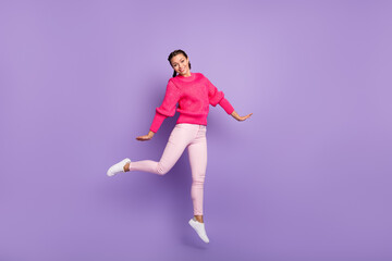 Full size photo of stunning positive young woman wear pink sweater trousers jump air isolated on violet color background
