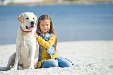 Child with a dog in nature. Little girl with a labrador retriever by the sea. High quality photo.