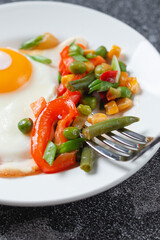 Fried eggs and vegetables in a white plate on a gray concrete stone table for breakfast, close up