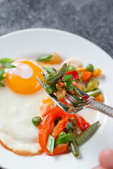 Fried eggs and vegetables in a white plate on a gray concrete stone table for breakfast, close up