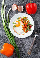 Fried eggs and vegetables in a white plate on a gray concrete stone table for breakfast