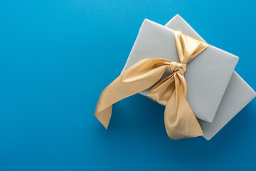 Gray gift boxes with golden bow on a blue background, birthday or valentine concept, top view, copy space