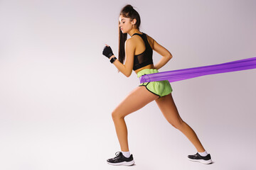 Sporty girl in top and sharts doing exercises with a harness of resistance on a white background with empty side space.