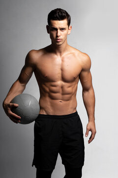 Front image of a handsome young fitness strong man bare-chested muscular sportsman basketball player isolated on grey background.