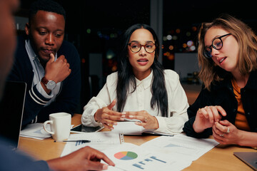 Young Group of multi ethnic business team analyzing financial documents with each other at night before a deadline