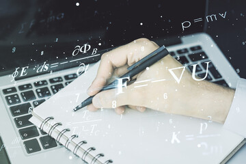 Creative scientific formula hologram with hand writing in notepad on background with laptop,...