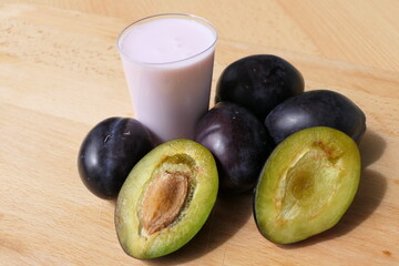 Sliced and whole plums on the wooden table and a fresh smoothie made from them