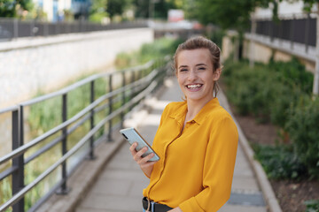 portrait of young laughing woman with yellow blouse and telephone in her hand