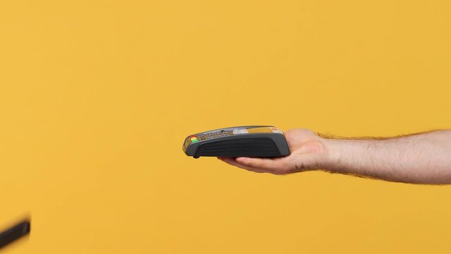 Cropped close up man male hold in hand wireless modern bank payment terminal to process acquire credit card payments pay use smart mobile phone isolated on yellow background studio. Commercial mock up