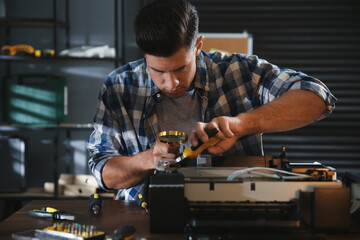 Repairman with magnifying glass and pliers fixing modern printer in office
