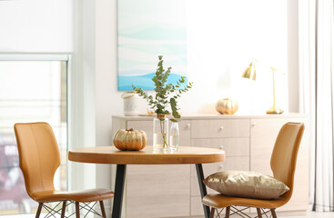 Beautiful living room interior with eucalyptus branches and decorative pumpkin on table