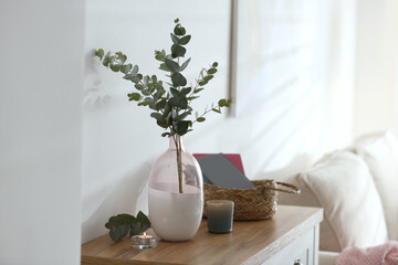 Vase with fresh eucalyptus branches on cabinet in room. Interior design © New Africa