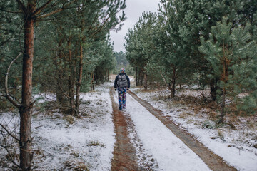 Obraz premium Sporty woman with bag walks on the road in snowy pine forest 