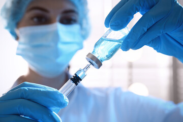 Woman filling syringe with vaccine from vial on blurred background, closeup