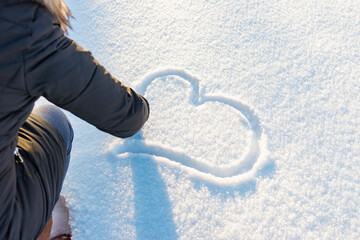 Woman drawing a heart on a snow.A woman wears blue gloves.Walentines day concept.
