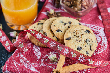 Chocolate chips cookies on red tablecloth with a glass of juice and cinnamons