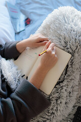 Mujer joven caucásica escribiendo en una libreta con un lápiz encima de la falda tapada con una...