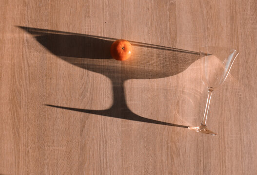 Wine transparent glass and sun shadow with an orange mandarin on a beige background. Aesthetic   minimal romantic concept. 
