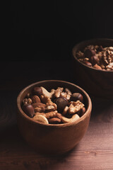 Bowl with mixed nuts on dark wooden table. Healthy organic food. Close up, vertical
