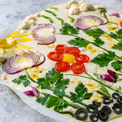 Beautiful bright focaccia decorated with vegetables. Focaccia art of natural bread leaven before baking.