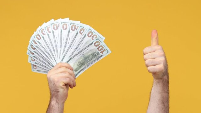 Cropped close up man male hand arm hold fan of cash money in dollar banknotes showing winner gesture clenching fist celebrate isolated on yellow background studio. Copy space commercial promo mock up