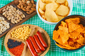 Assorted snacks, bowl of chips and a plate of sausages on a blue table