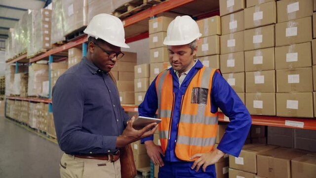 Multiethnic male worker and manager shake hands together after the discussion using digital tablet in large distribution warehouse