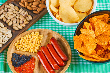 Assorted snacks, bowl of chips and a plate of sausages on a blue table