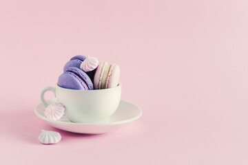 Cup with french macarons and marshmallows on a pink pastel background.