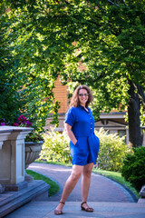 Beautiful young smiling woman in sunglasses in city park at summer day wearing dress and looking to the camera